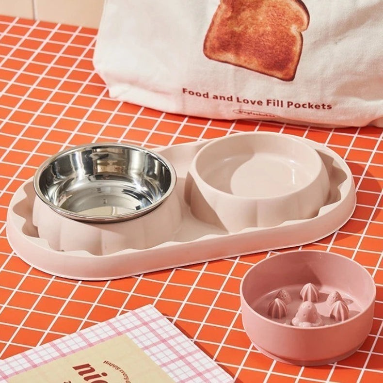 Double gamelle Bofélin rose avec bol anti-glouton en inox et support plastique sur fond à carreaux orange
