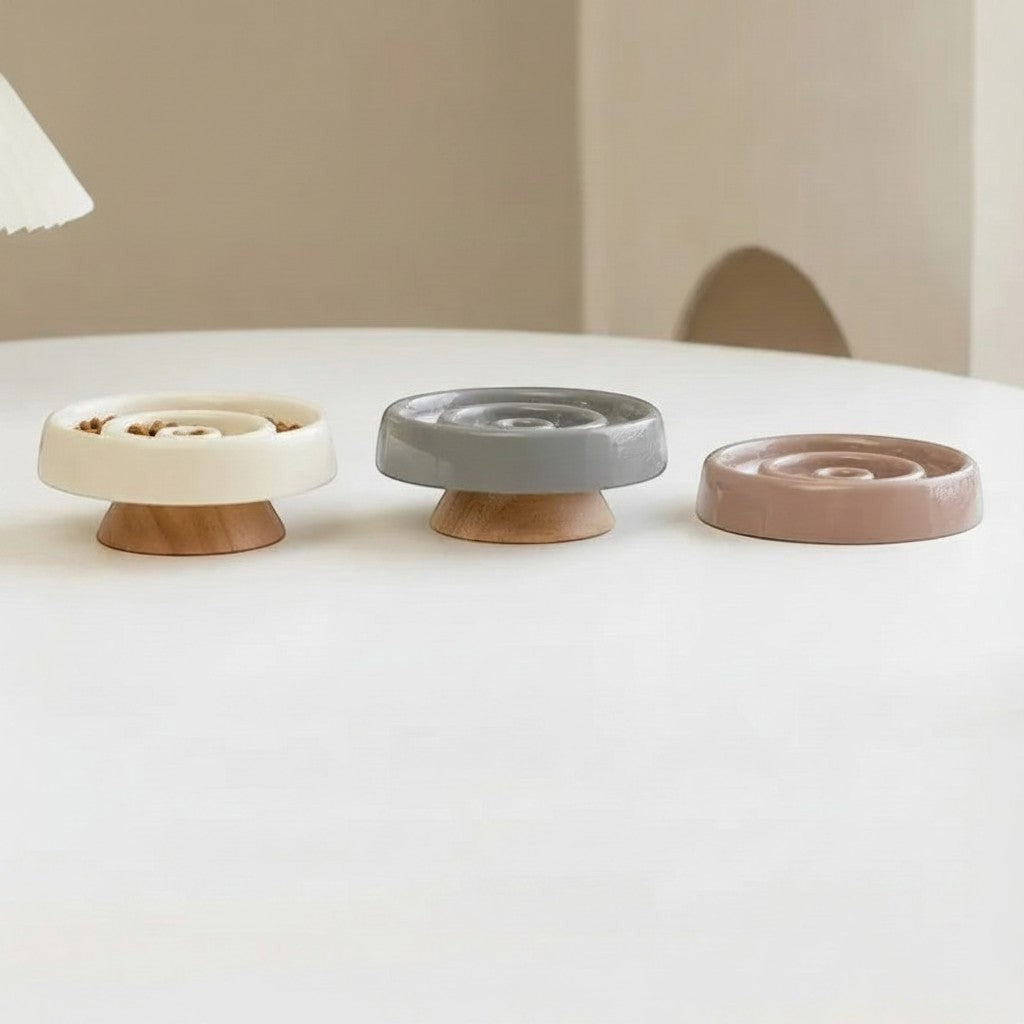 Trois gamelles anti-glouton Bofélin en céramique beige, grise et brune avec pied en bois sur une table blanche.
