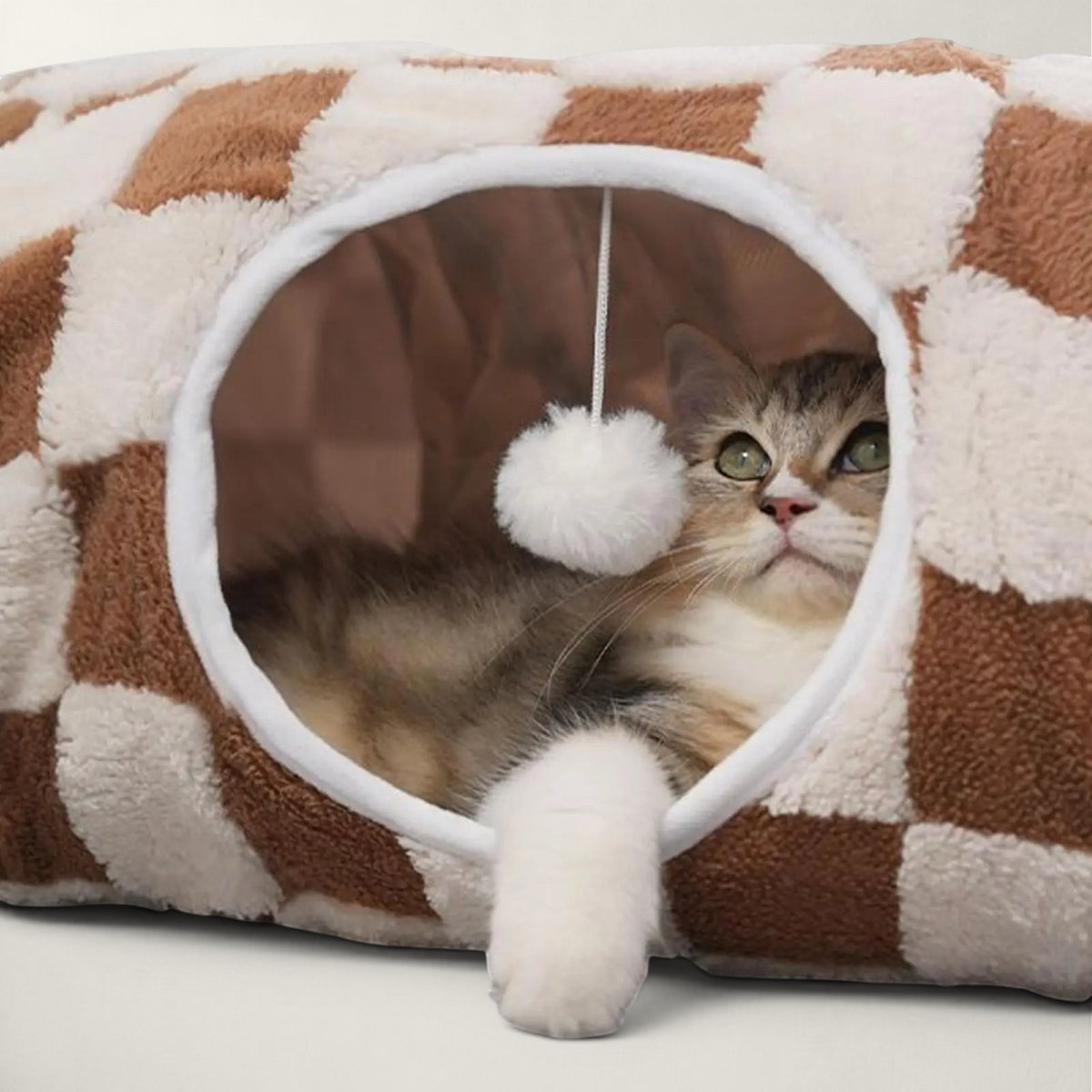 Tunnel pour chat Bofélin en velours doux taupe et blanc à damier avec chat jouant avec une balle suspendue